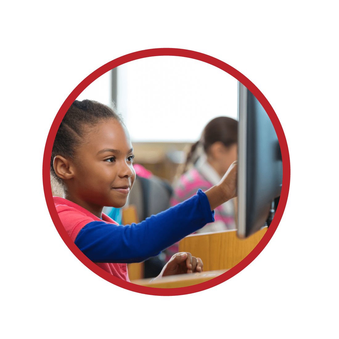 Elementary age African American little girl is smiling while using a desktop computer in public school library or computer lab. Diverse students are wearing casual clothing. Child is pointing at computer monitor screen while working on school assignment.