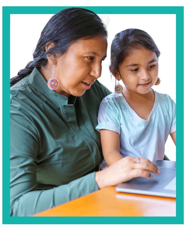 A woman and a young girl work together on a notebook computer.